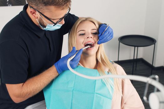 Portrait of a dentist in eyeglasses who treats teeth of young blond woman patient.