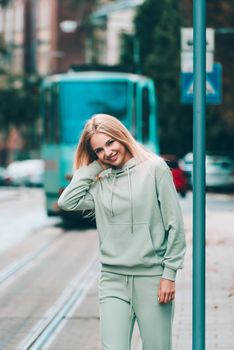 Stylish beautiful young blond woman in a light green tracksuit posing on the street. Attractive girl model posing outdoors. Fitness lady