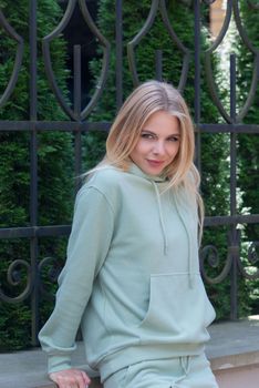 Stylish beautiful young blond woman in a light green tracksuit posing on the street. Attractive girl model posing outdoors. Fitness lady