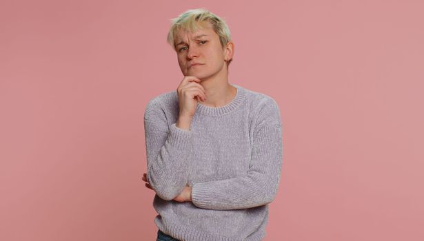 Thoughtful clever millennial woman with short hair rubbing chin and looking aside with pensive expression, pondering a solution, doubting question. Young girl on pink background. Lgbt lesbian people