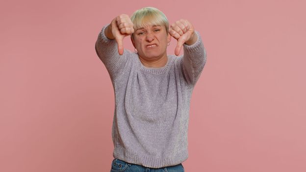 Dislike. Upset unhappy lovely woman with short hair showing thumbs down sign gesture, expressing discontent, disapproval, dissatisfied, dislike. Young girl on pink background. Lgbt gay lesbian people