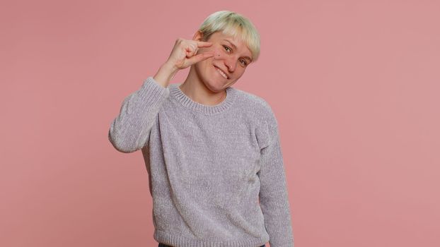Need some more, please give me. Woman with short hair showing a little bit gesture with sceptic smile, showing minimum sign measuring small size. Young girl on pink background. Lgbt gay lesbian people