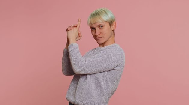 Woman with short hair pointing around with finger gun gesture, looking confident, making choice, shooting killing with hand pistol right on target. Girl on pink background. Lgbt gay lesbian people