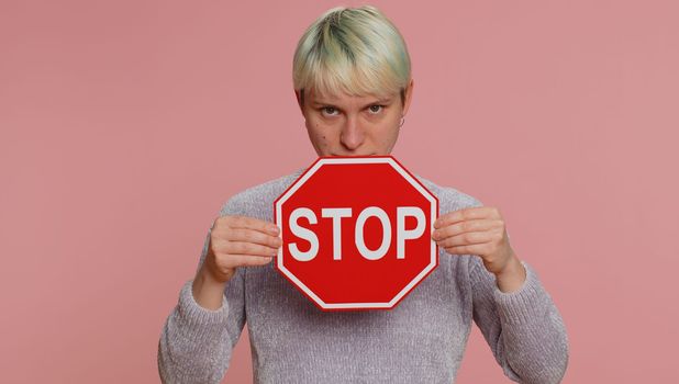 Serious woman say No, hold inscription text banner red No stop danger sign, warning of finish, prohibited access declining communication, trouble, protest. Girl with short hair on pink background