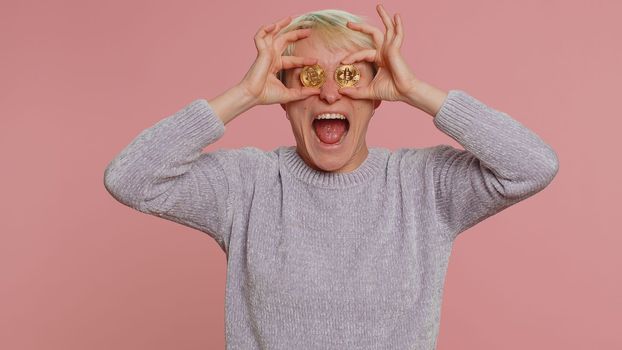 Woman with short hair showing golden bitcoins BTC. Achievement career wealth, cryptocurrency investment, mining, future technology. Girl fooling, making faces on pink background. Happy businesswoman