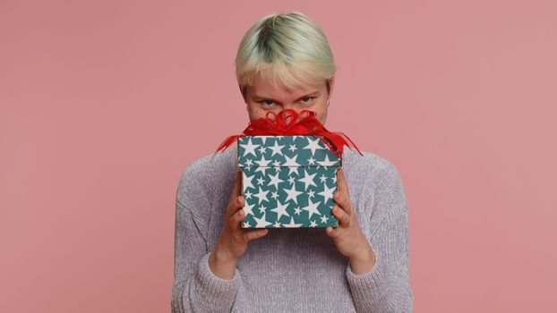 Positive smiling woman presenting birthday gift box stretches out hands, offer wrapped present career bonus, celebrating party. Young girl isolated on pink studio background. Lgbt gay lesbian people