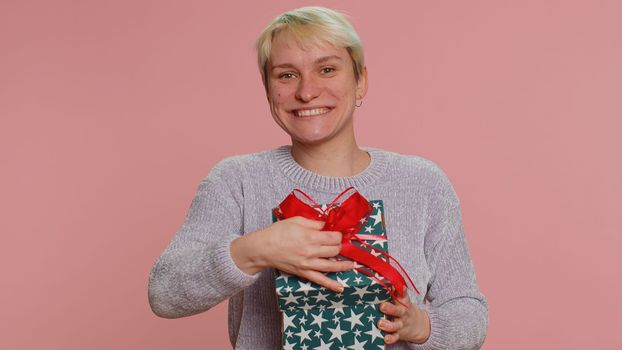 Cheerful woman with short hair opening gift box and smiling joyfully, looking amazed satisfied with nice present, unexpected birthday surprise. Young girl on pink background. Lgbt gay lesbian people