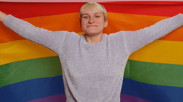 Millennial woman with short hair posing with rainbow LGBT flag celebrate parade show tolerance same sex marriages. Young girl isolated on pink studio background. Bisexuality gay lesbian people concept