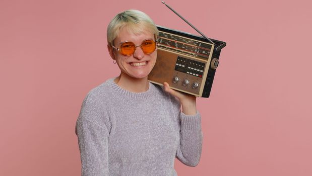 Millennial woman with short hair using retro tape record player to listen music, disco dancing of favorite track, having fun, entertaining, fan of vintage technologies. Young girl on pink background