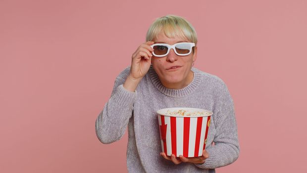 Excited woman with green short hair eating popcorn, watching tv serial, sport game, film, online social media movie content. Young girl in 3D glasses enjoying domestic entertainment on pink background