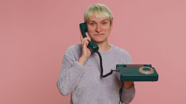 Hey you, call me back. Millennial woman with short hair talking on wired vintage telephone of 80s, says hey you call me back. Young girl isolated on pink background. Lgbt gay lesbian people concept