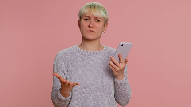 Hipster woman with short hair use mobile cell phone typing browsing, loses becoming surprised sudden lottery results, bad fortune, loss, fail. Young girl isolated alone on pink studio wall background