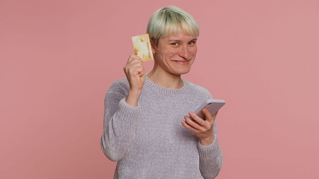 Sincere woman customer using credit bank card and smartphone while transferring money, purchases online shopping, payment. Finance and internet. Young girl on pink background. Lgbt gay lesbian people