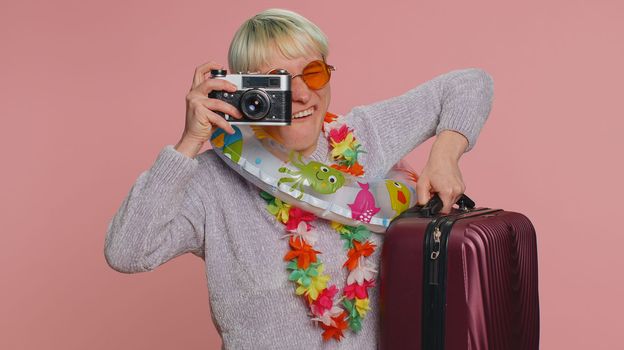 Millennial woman tourist photographer with short hair taking photos on retro camera and smiling. Travel, summer holiday vacation. Young girl isolated on pink studio background. Lgbt gay lesbian people