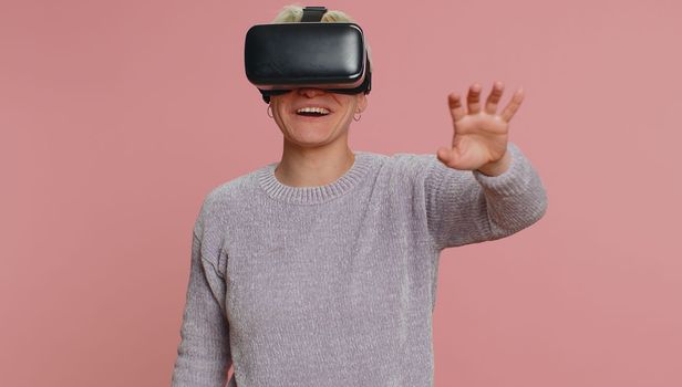 Young woman using headset helmet to play simulation game app online. Watching virtual reality 3D 360 video content. Caucasian one girl in VR goggles on studio pink background. Futuristic technology