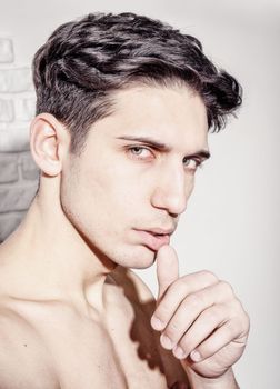 Handsome young man's headshot against white wall with a hand on his chin, looking at camera to a side