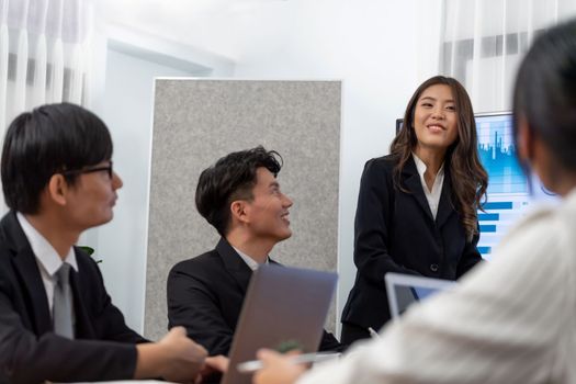 Confidence and young asian businesswoman give presentation on financial business strategy in dashboard report display on screen to colleagues in conference room meeting as harmony in workplace concept