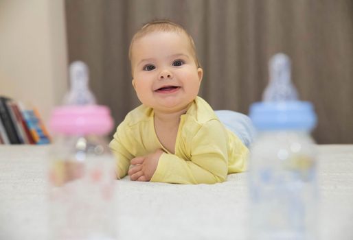 cute baby smiling lying on the bed and looks between two children bottles