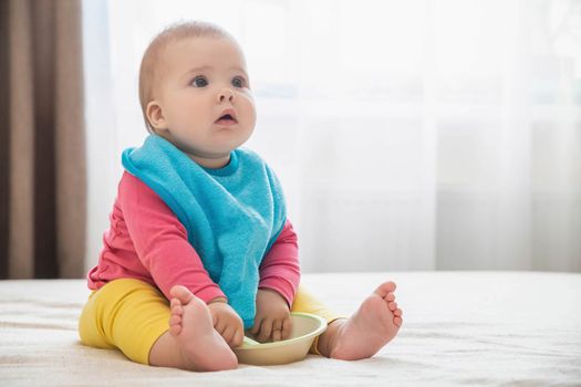 charming baby in bib with a plate waiting for lunch.