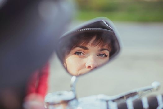 Girl in a helmet looks in a motorcycle mirror.