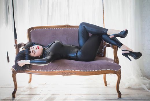 luxurious brunette in a black leather suit lies on an old sofa.