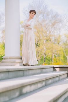 beautiful slim woman in a long evening dress stands at the columns.