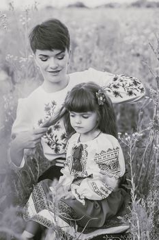 Mom in Ukrainian national dress braids her daughter's hair in the field. Retro photo. Focus on daughter