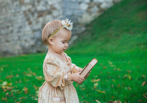 charming baby in princess costume with a crown on head is carries a wooden box