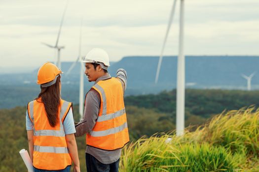 Male and female engineers working on a wind farm atop a hill or mountain in the rural. Progressive ideal for the future production of renewable, sustainable energy.