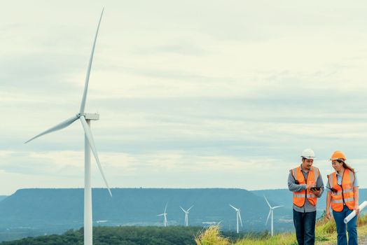 Male and female engineers working on a wind farm atop a hill or mountain in the rural. Progressive ideal for the future production of renewable, sustainable energy.