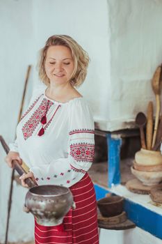 Hostess in embroidered clothes pulled a pot of food out of the oven. Ancient Ukrainian life