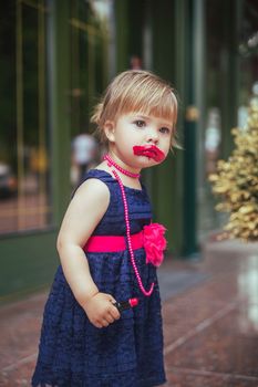 Adorable baby in a dress paints lips with lipstick.