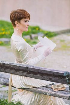 Retro photo of beautiful woman in golden dress writing letter with quill pen in the garden