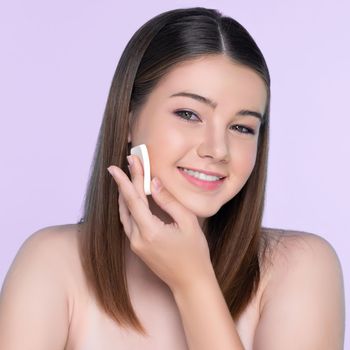 Facial cosmetic makeup concept. Portrait of young charming girl applying dry powder foundation. Beautiful girl smiling with perfect skin putting cosmetic makeup on her face.