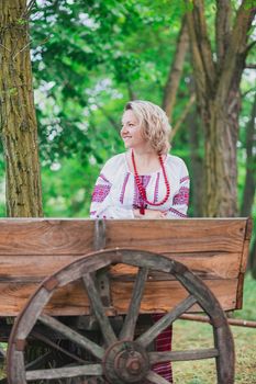 Beautiful peasant woman in embroidered clothes laughing near the cart.