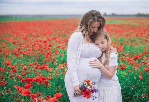 pregnant mother with her eldest daughter dressed in white dresses is cuddle in the poppy field