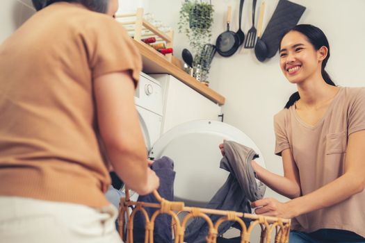 Daughter and mother working together to complete their household chores near the washing machine in a happy and contented manner. Mother and daughter doing the usual tasks in the house.