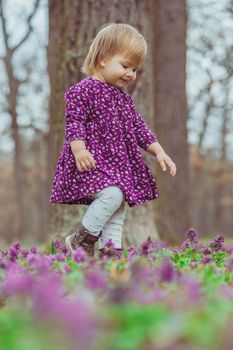 blond baby in a colored dress running in a forest glade with flowers.