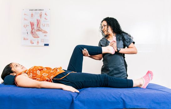 Professional physiotherapist assisting patient in leg rehabilitation. Modern leg rehabilitation physiotherapy. Worker in modern physiotherapy assisting female patient.
