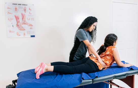 Physiotherapist assisting lumbar treatment to lying patient. Young physiotherapist assisting female patient with lower back pain, Woman performing lumbar physiotherapy to patient
