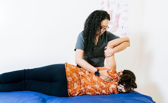 Woman doing back rehabilitation physiotherapy. Young physiotherapist rehabilitating back to patient lying on her side. Therapeutic back treatment and rehabilitation concept