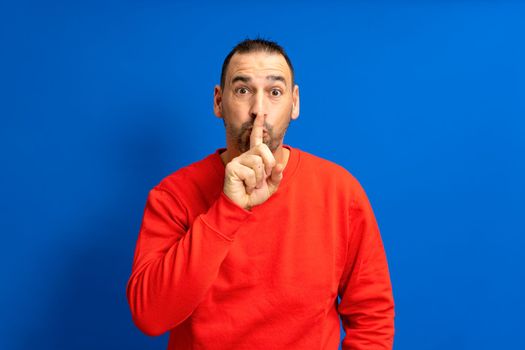 Serious handsome bearded hispanic man puts his index finger to his lips, tries to keep conspiracy, looks aside and says: Shh, be quiet please. Isolated shot of attractive man shows silence sign