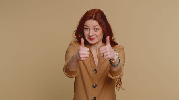 Like. Hipster pretty redhead woman in blouse raises thumbs up agrees with something or gives positive reply recommends advertisement likes good. Young girl isolated alone on beige studio background