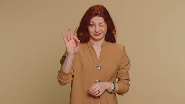 Ok. Joyful happy redhead woman in blouse looking approvingly at camera showing approve feedback gesture like sign positive something good. Young girl on beige studio background. People sincere emotion