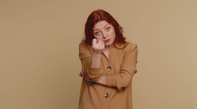 Angry aggressive redhead woman showing fig negative gesture, you dont get it anyway. Rapacious, avaricious, acquisitive. Body language. Refusal fig sign. Greedy avaricious girl on beige background