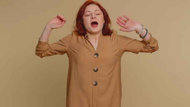 Tired redhead woman yawning, sleepy inattentive feeling somnolent lazy bored overworked gaping suffering from lack of sleep. Young exhausted ginger girl isolated alone on beige studio background