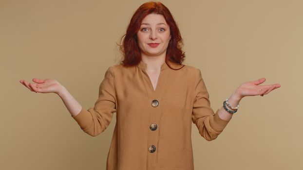 I dont know what to say. Confused woman feeling embarrassed about ambiguous question, having doubts, no idea, being clueless and uncertain. Young redhead girl isolated on beige studio wall background