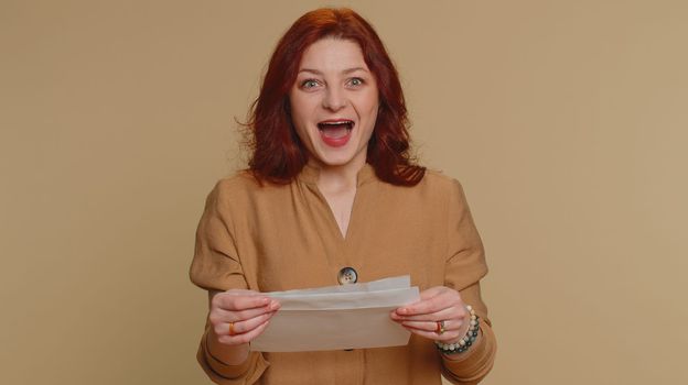 Young redhead student woman open envelope take out letter reads it feel happy. Girl career growth advance promotion, bank loan approve, monetary award, long-awaited invitation great news, lottery win