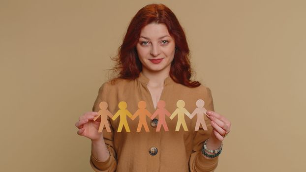 Woman showing multiracial different skin color human shape cut out of paper, concept of teamwork, partnership, community, unity, people support love, against racism. Young girl on beige background