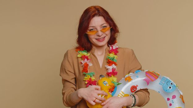 Traveler tourist young woman celebrating, dancing fooling with swimming inflatable duck toy. Concept summer vacation, journey, trip to seaside. Redhead girl in sunglasses on beige studio background